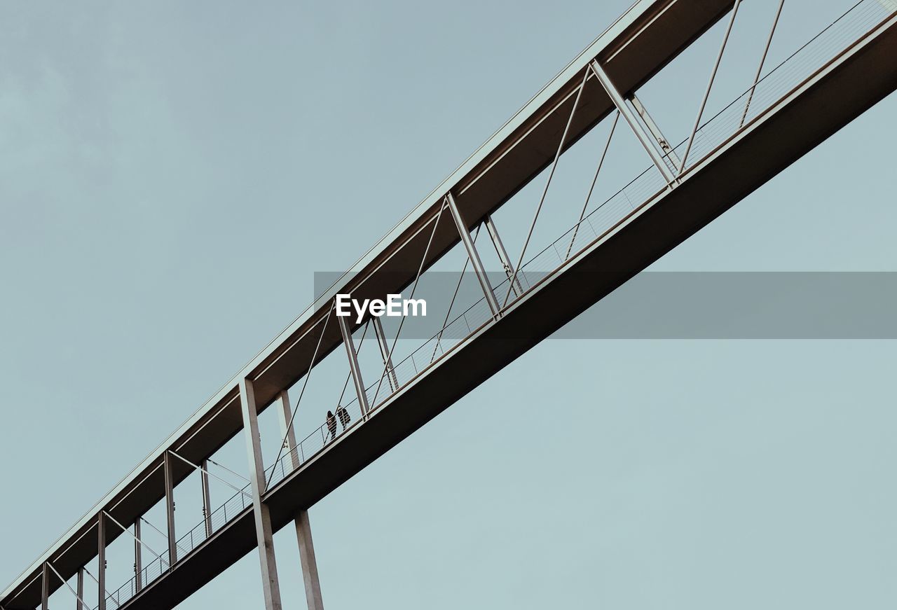 Low angle view of people on footbridge against clear sky