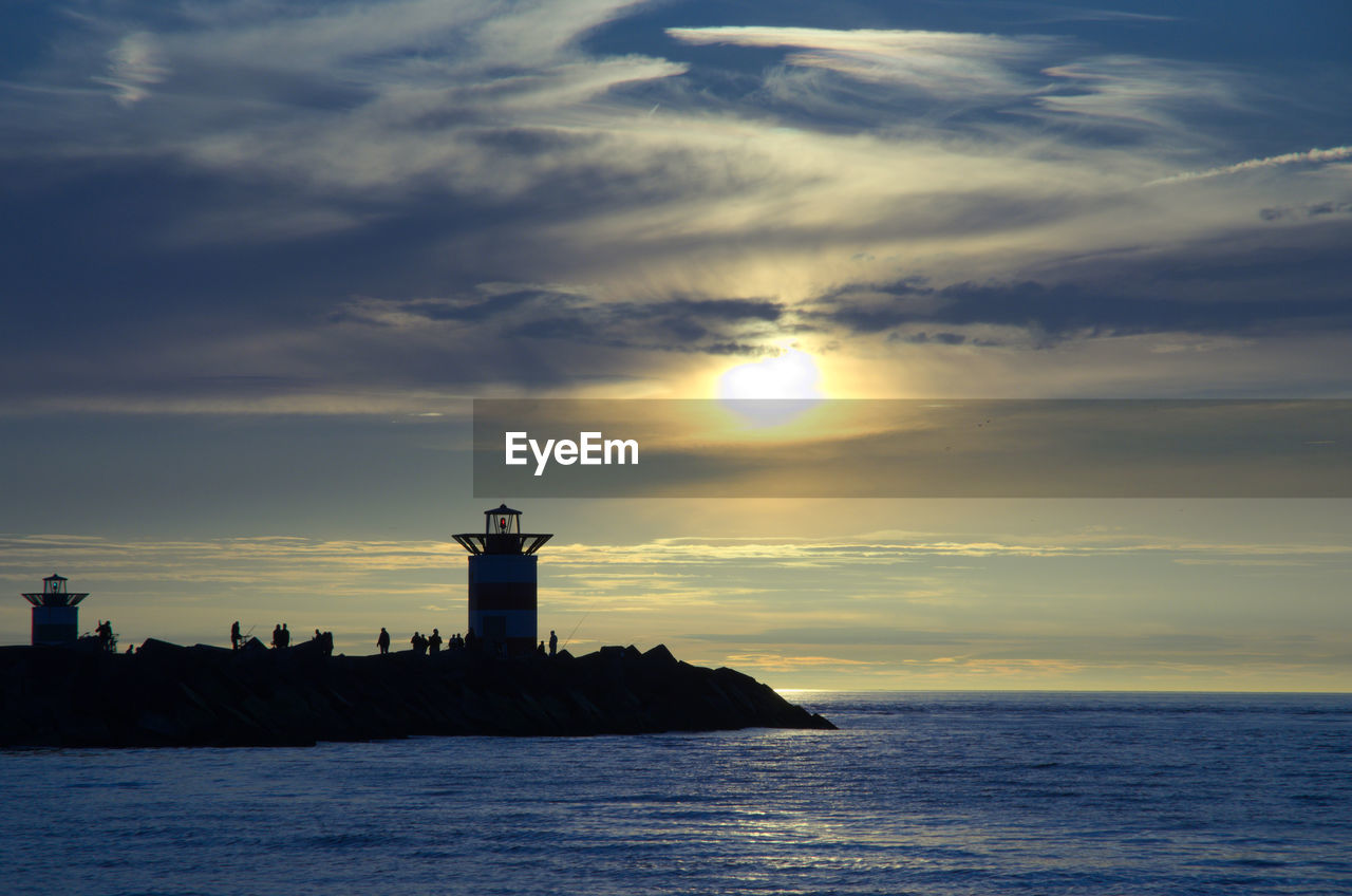 Silhouette of lighthouse by sea against sky during sunset