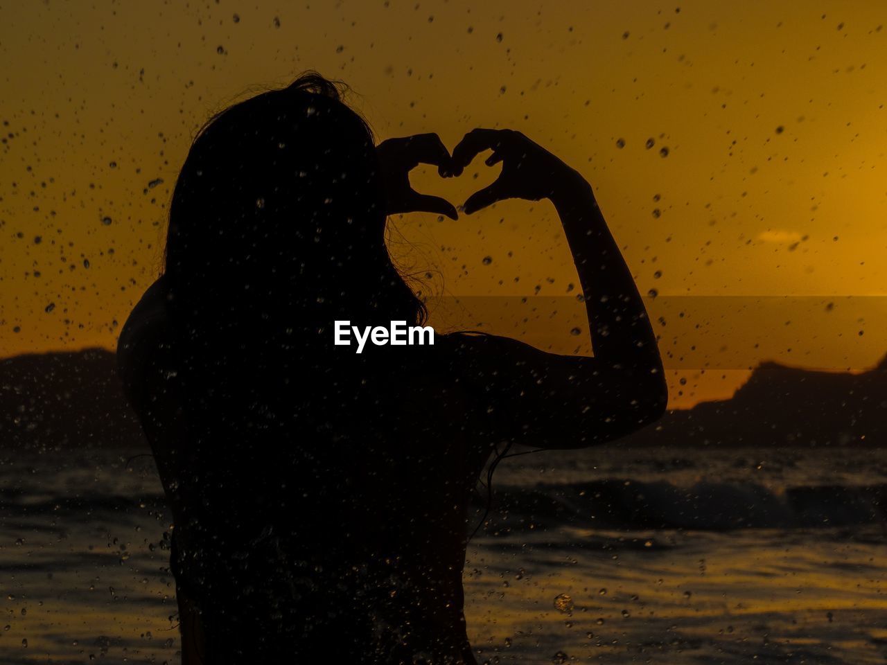 Rear view of silhouette woman making heart shape at beach during sunset