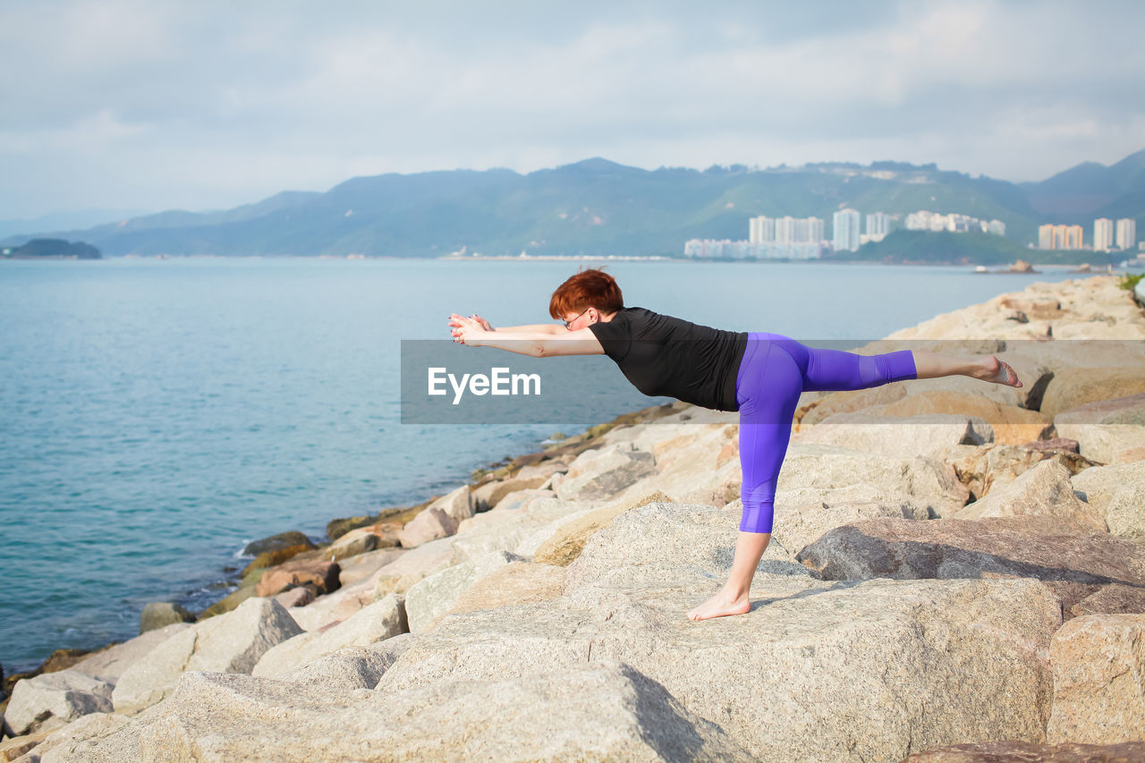 Full length of mature woman practicing yoga on rocks at beach