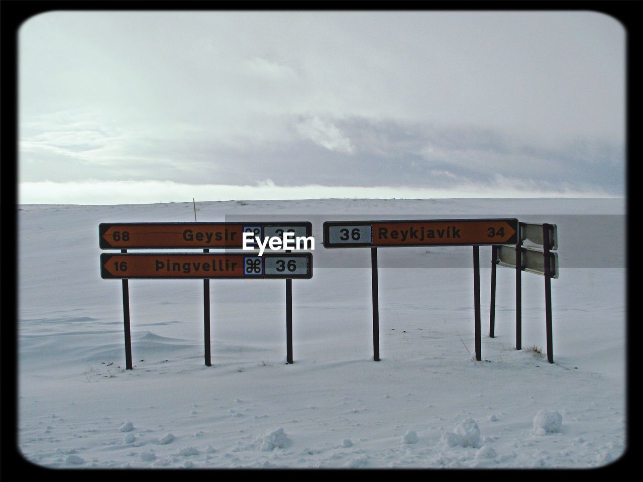 Sign board on snow covered field against sky