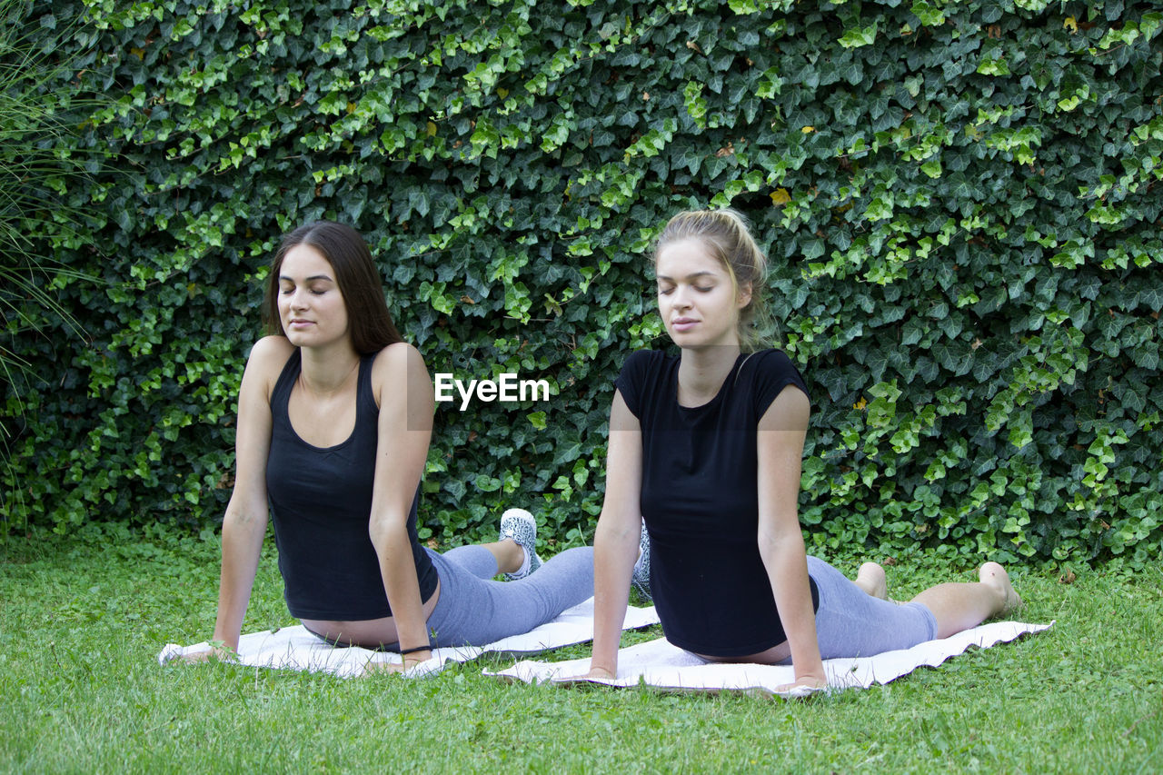 Women with eyes closed exercising against plants in park