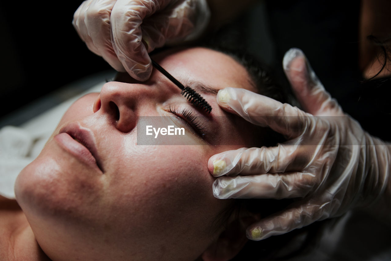 Crop anonymous cosmetician in latex gloves curling eyelashes of female patient during lash lift procedure in salon