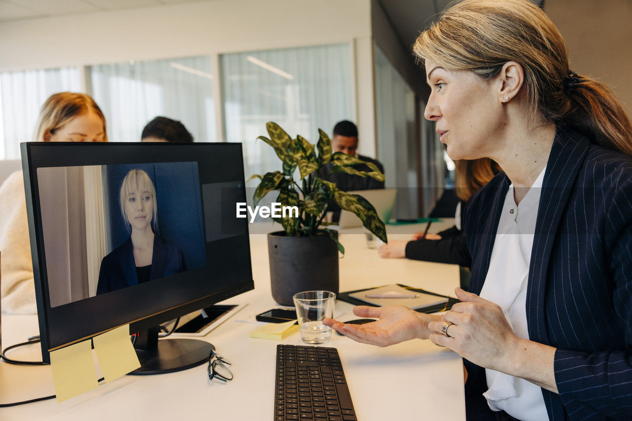 Businesswoman doing video call with colleague on computer at desk in coworking office