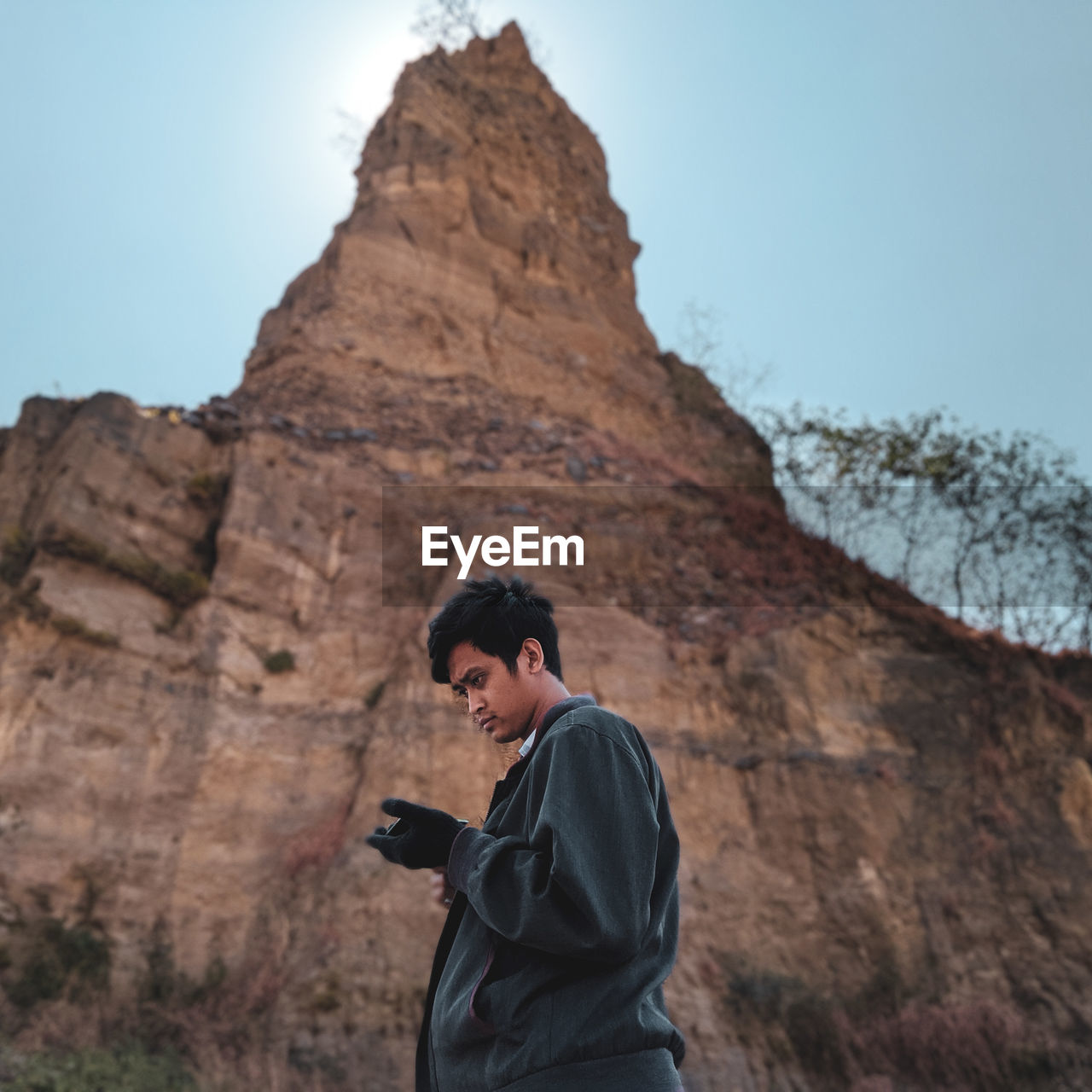 Side view of young man standing against rock formation and sky