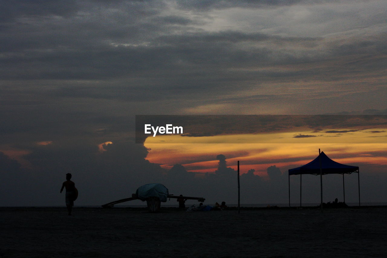 SILHOUETTE PEOPLE WALKING ON BEACH AGAINST SKY AT SUNSET