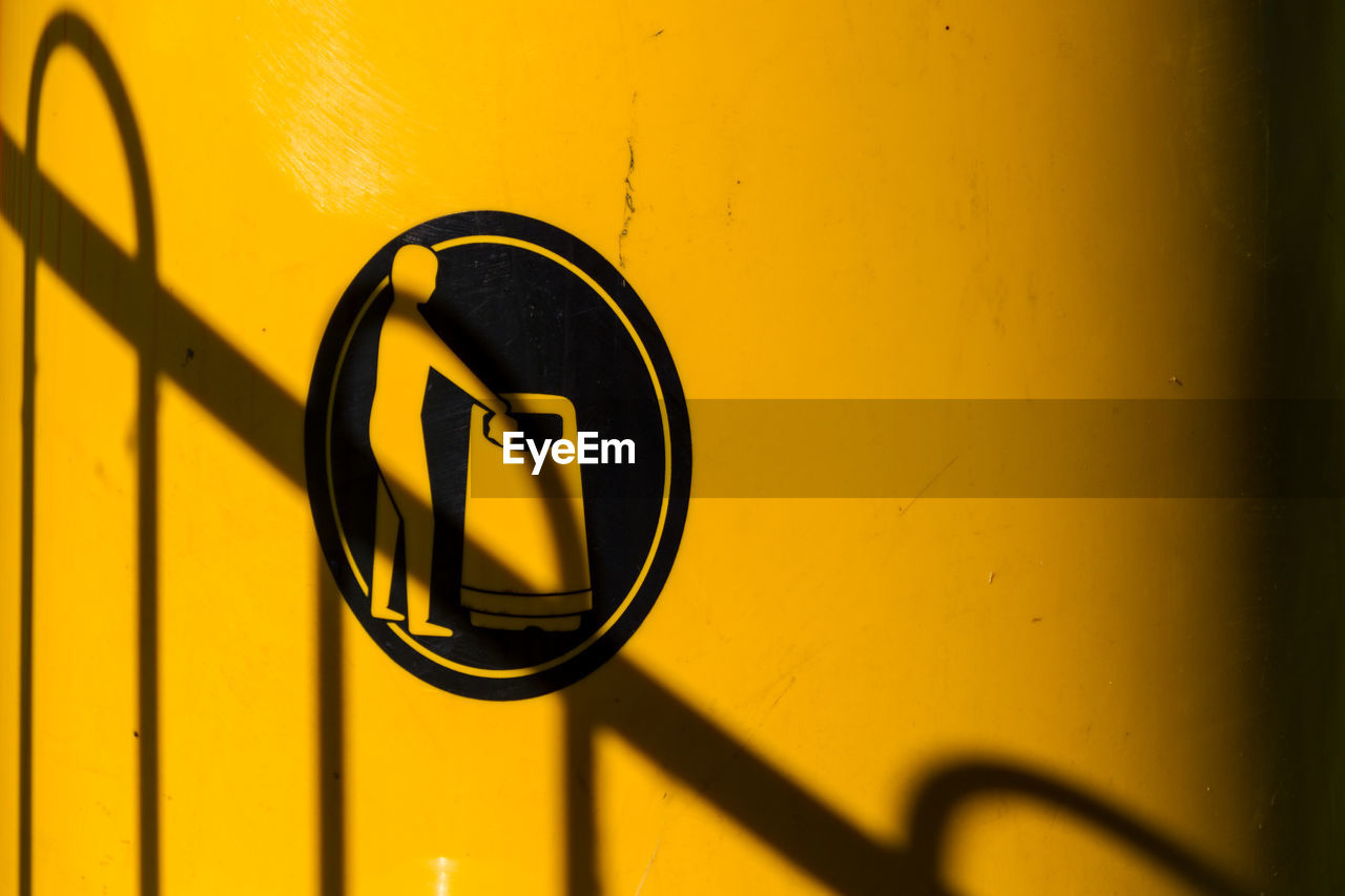 Close up of fence shadow on yellow litter bin with bin your litter logo