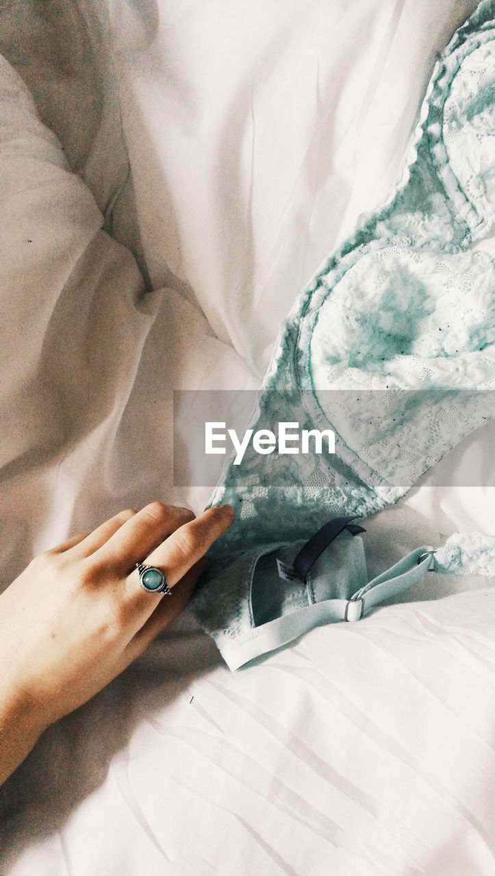 Cropped hand of woman holding lingerie on bed at home