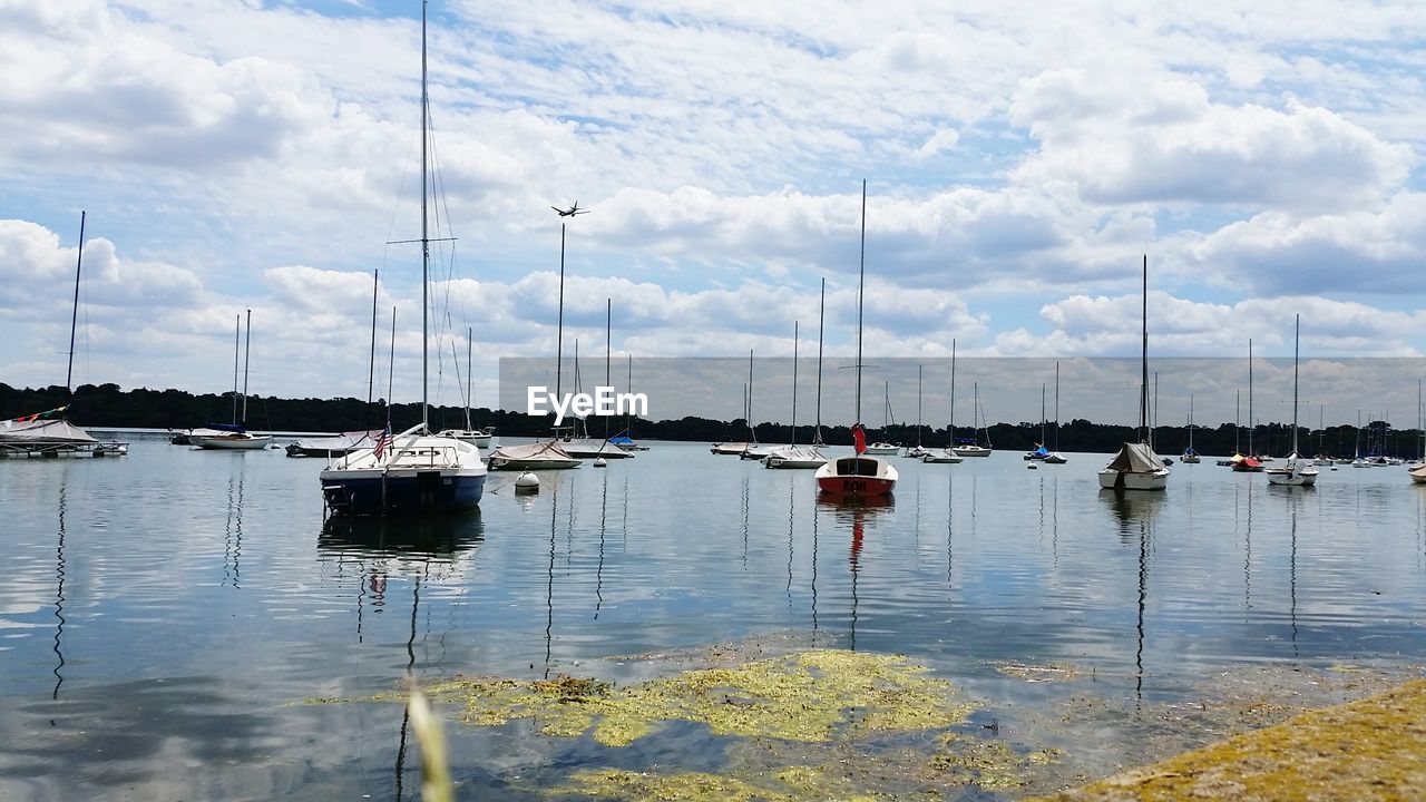 Scenic view of sailboats in water against cloudy sky