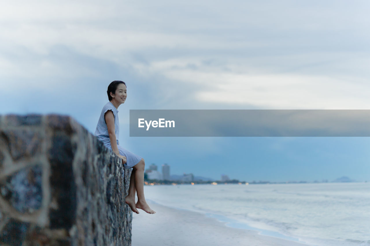 Woman sitting on wall and looking at the sea.