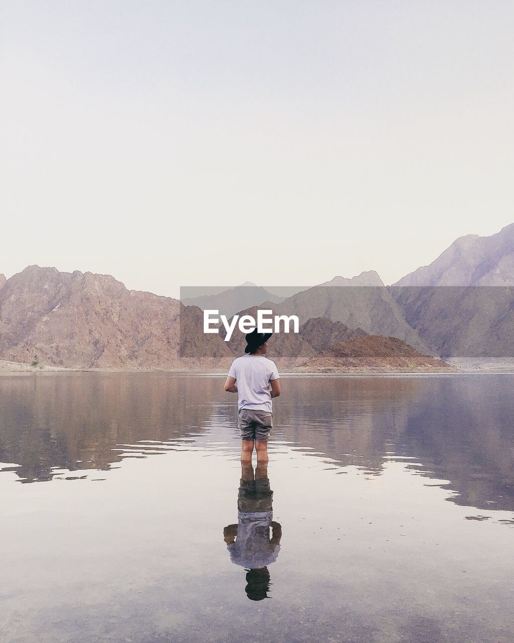 Rear view of man standing in lake against mountains