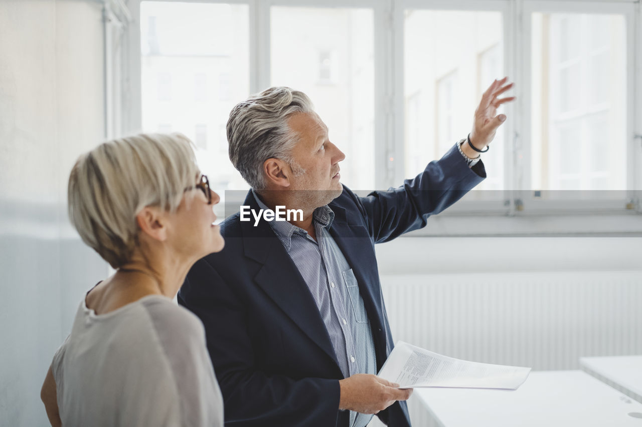 Mature businessman holding documents while discussing with female coworker in new office