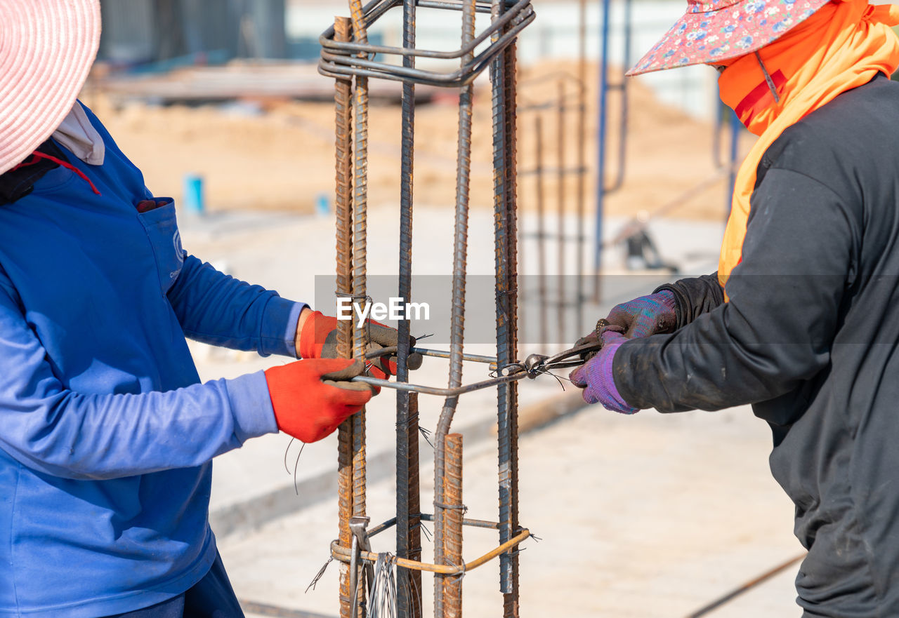 Two workers are tying wire to rebar to pour concrete poles in construction site.