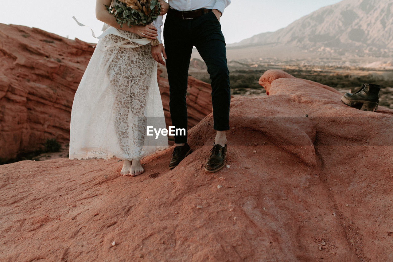 Low section of bride and groom standing on rock formation