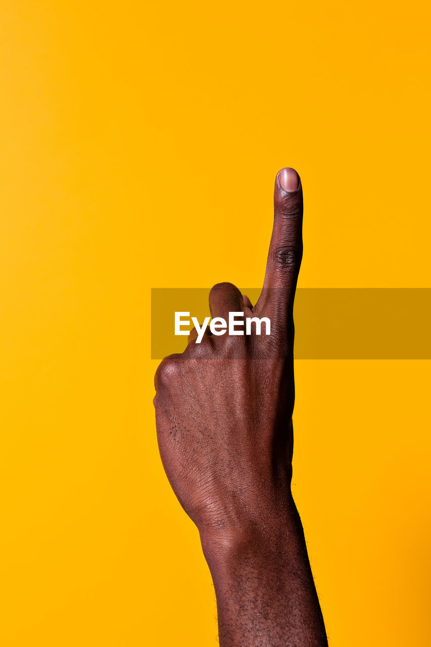 Crop forearm and hand of african-american man raising his index finger against yellow background