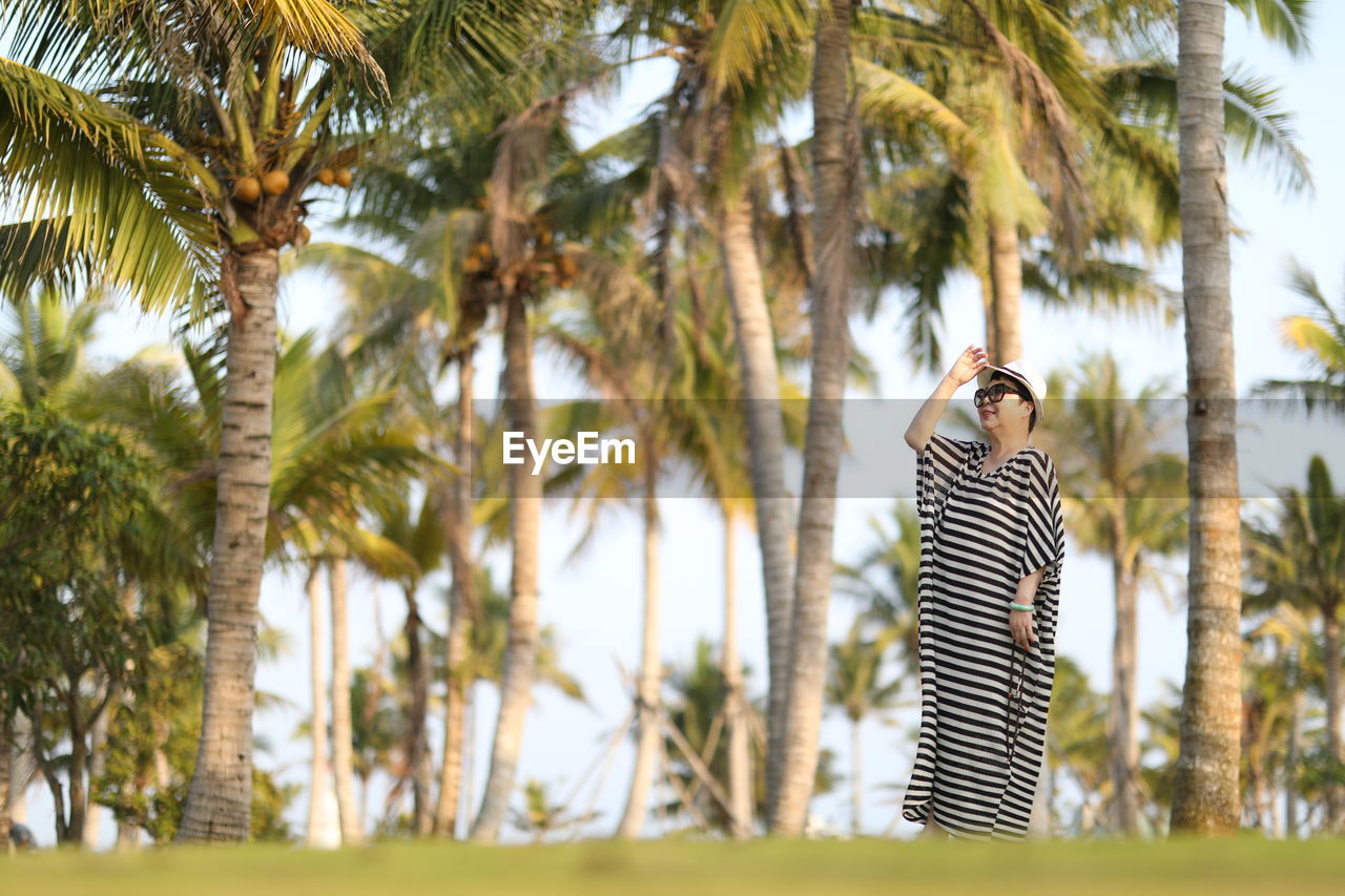 Woman standing on grass against palm trees