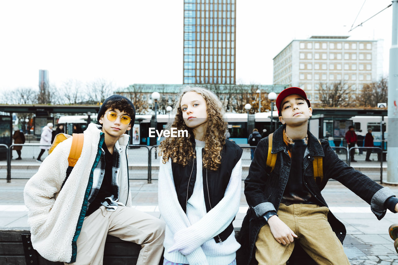 Portrait of multiracial male and female friends sitting on bench in city during weekend