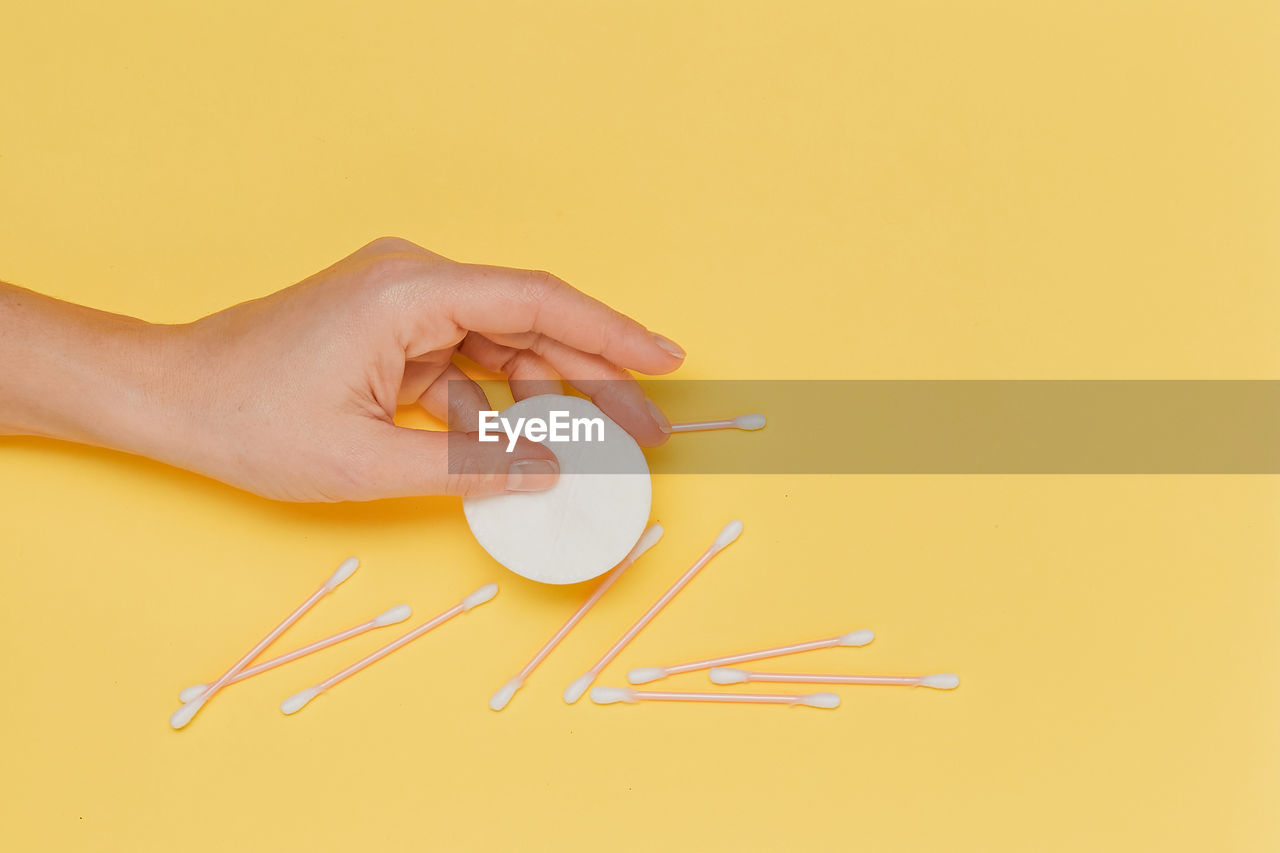 cropped hand of woman holding thermometer against yellow background