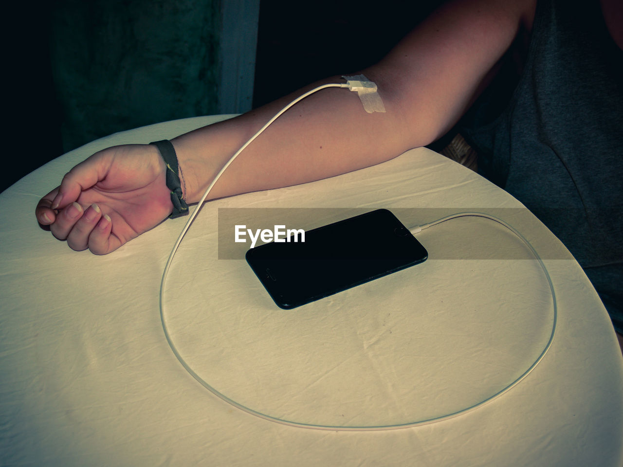 Midsection of woman with cable connected to hand sitting by table at home