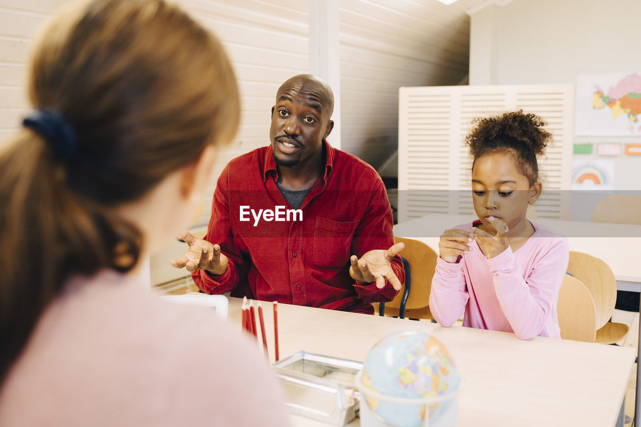 Surprised man sitting with son talking to teacher at classroom