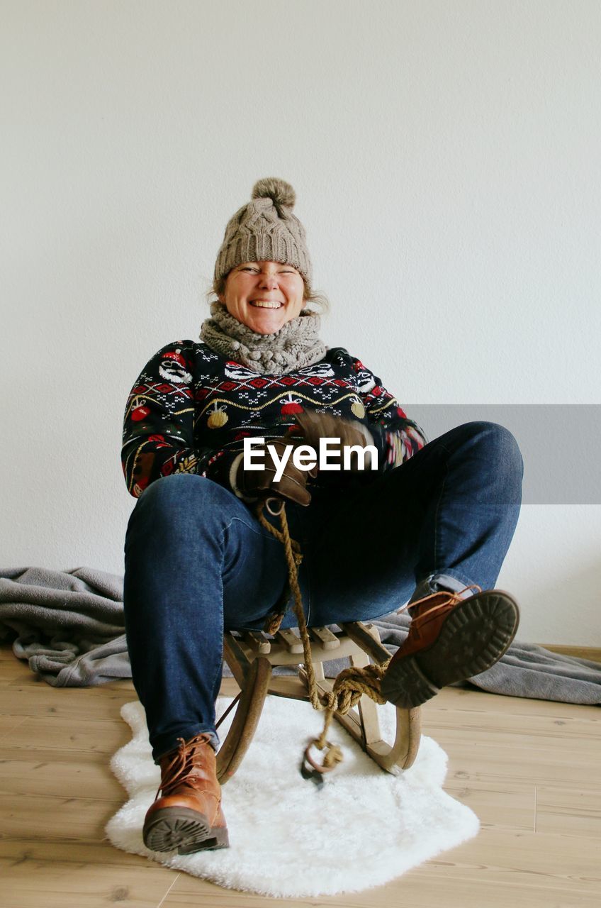 Young woman sitting on sled against wall