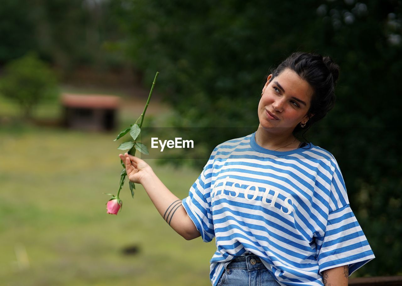 Young woman smiling with a rose in the garden.