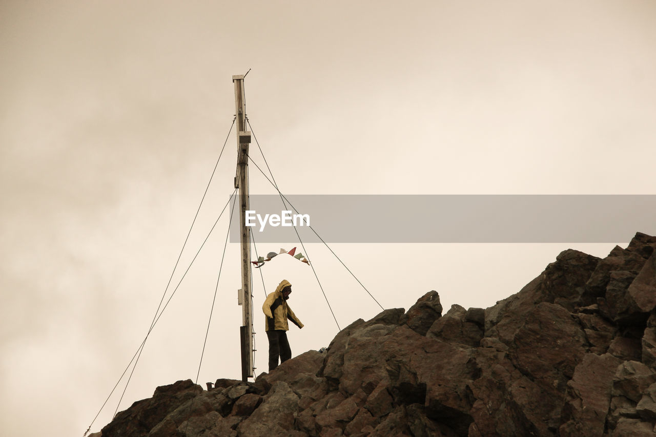 Low angle view of person standing on rock against sky