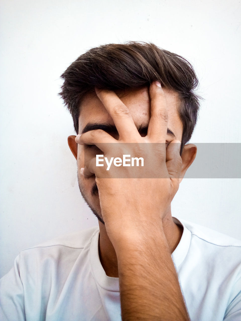Young man covering face with hand against white background