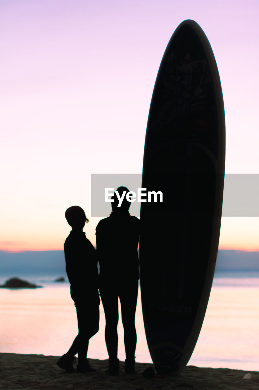 Silhouettes of two women with surfboard on the beach during sunset