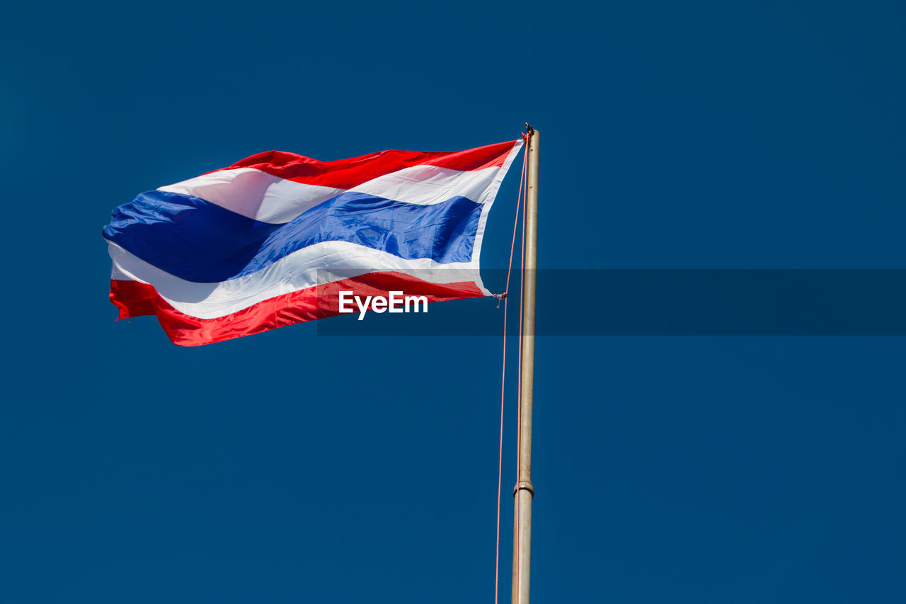 Low angle view of thai flag waving against clear blue sky
