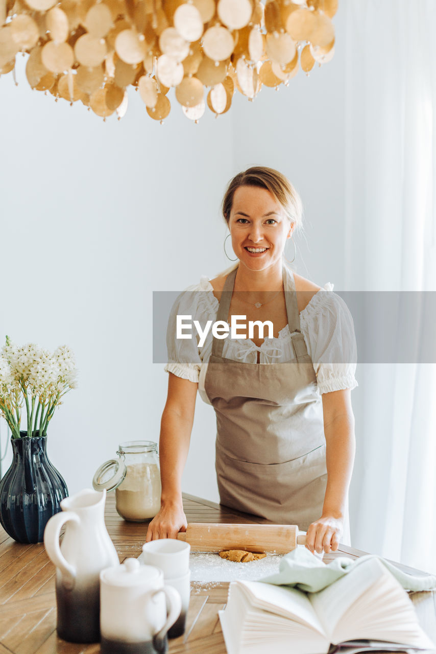 Woman rolling dough for cookies standing at kitchen looking at camera