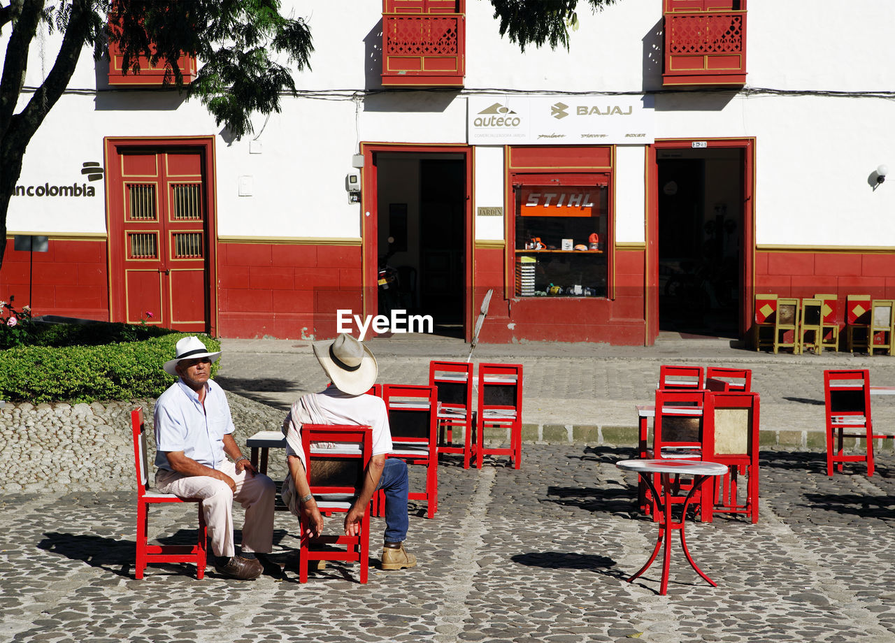 MAN SITTING ON CHAIR AGAINST BUILDING