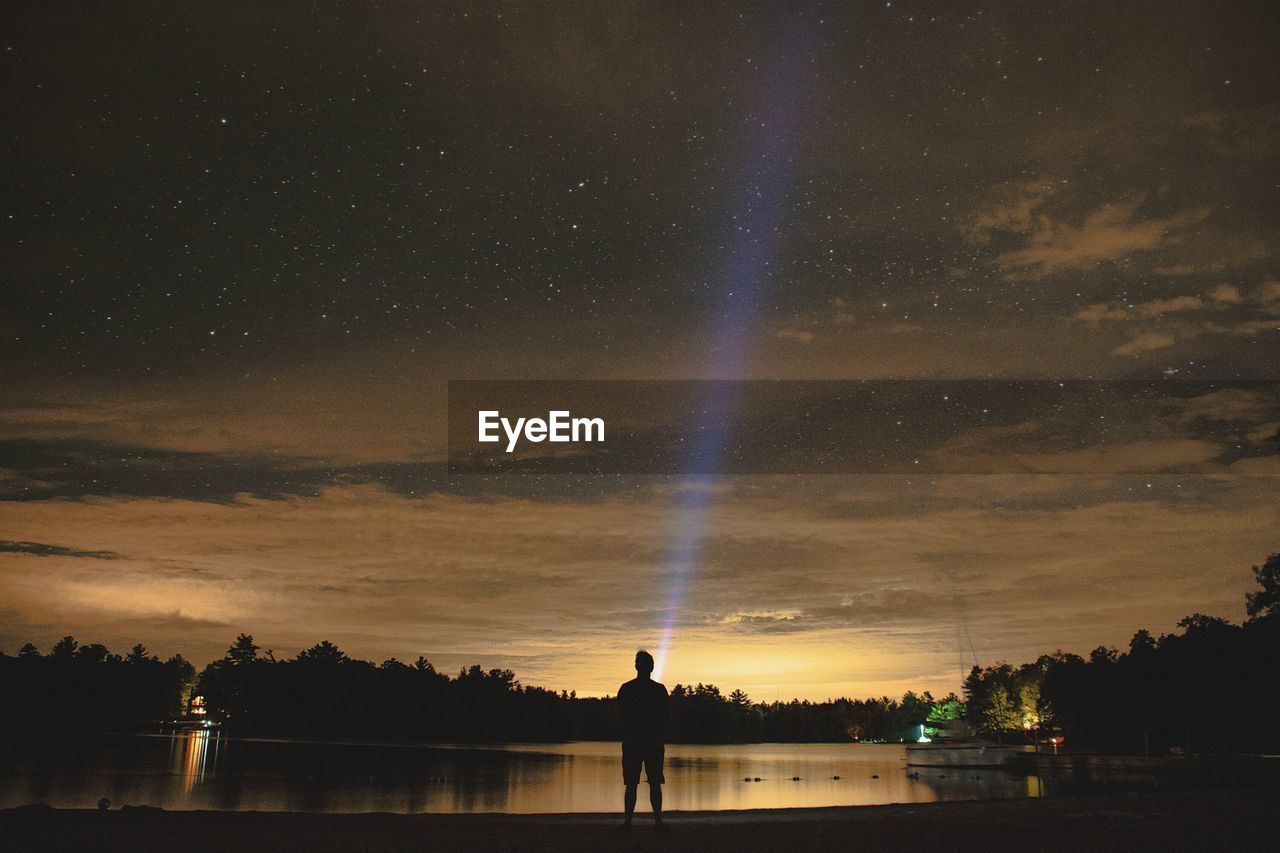 Young man painting with light by lake against starry sky