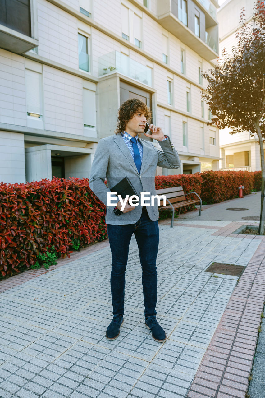 Businessman talking on smart phone while standing at sidewalk in city