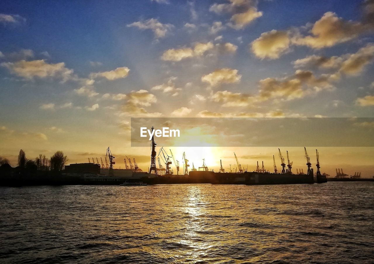 Silhouette cranes against sky during sunset