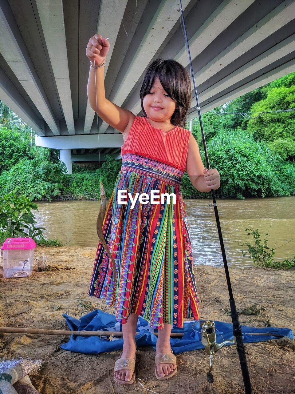 A girl holding a caught fish in front of a river.