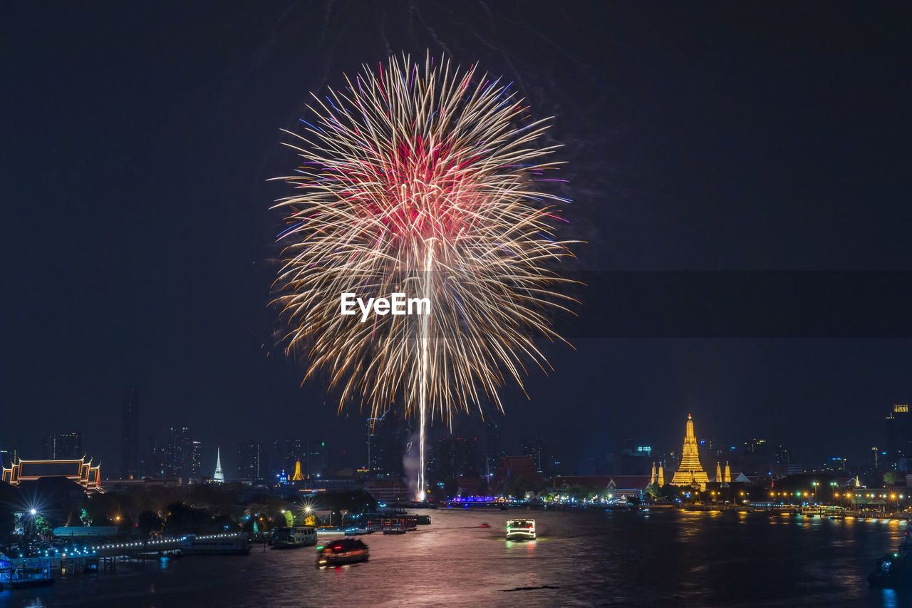 High angle view of river amidst city against firework display in sky at night
