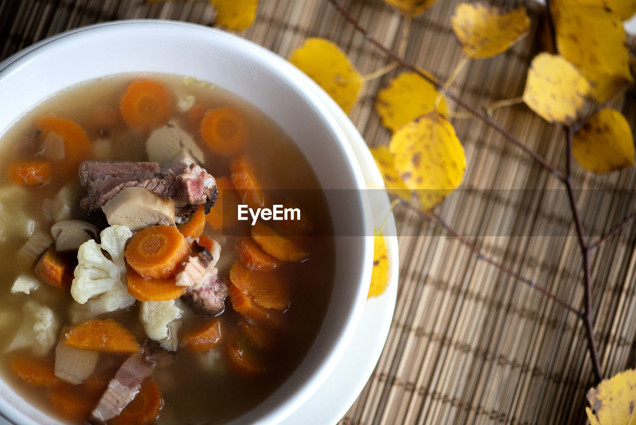 An overhead photo of a plate mushroom soup with boletus decorated with colorful autumn leaves