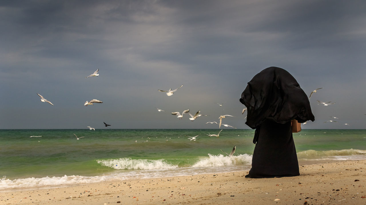 Rear view of woman standing at sea against sky