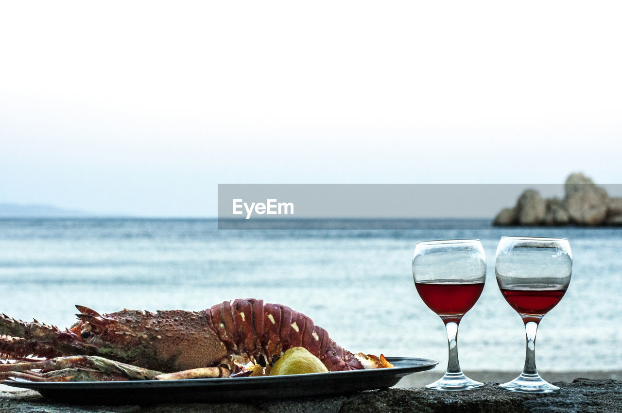 Close-up of lobster and drink on table by sea against clear sky