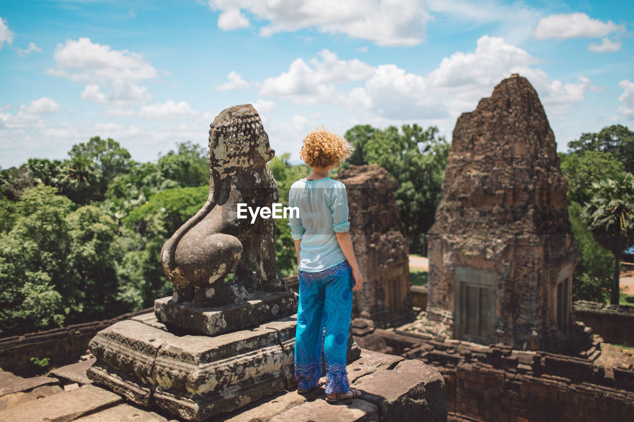 Woman standing by old statue at temple against sky