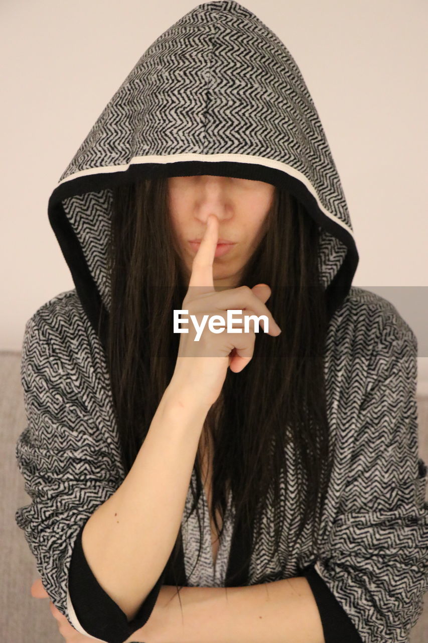 Woman wearing hood with finger on lips at home