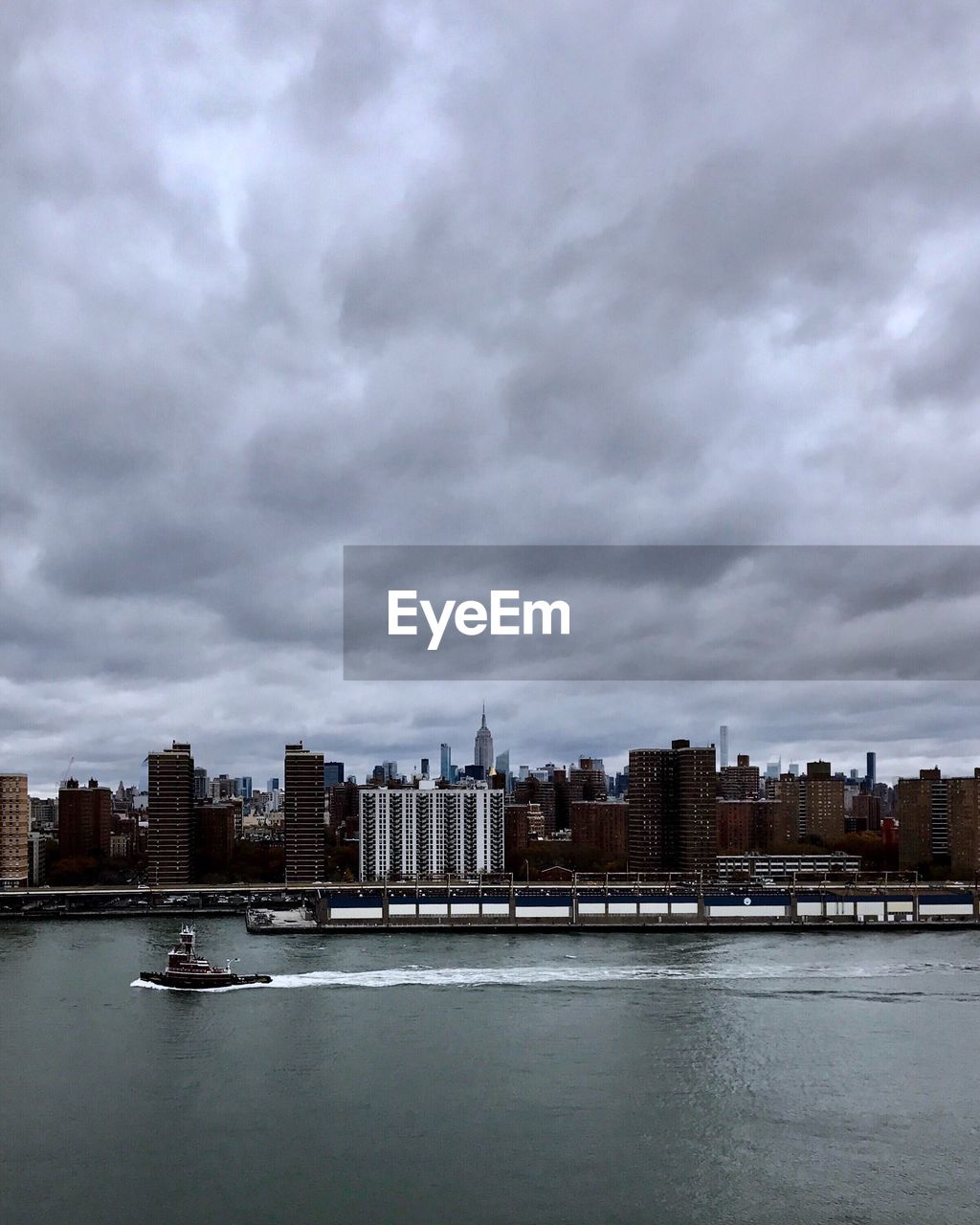 City at waterfront against cloudy sky