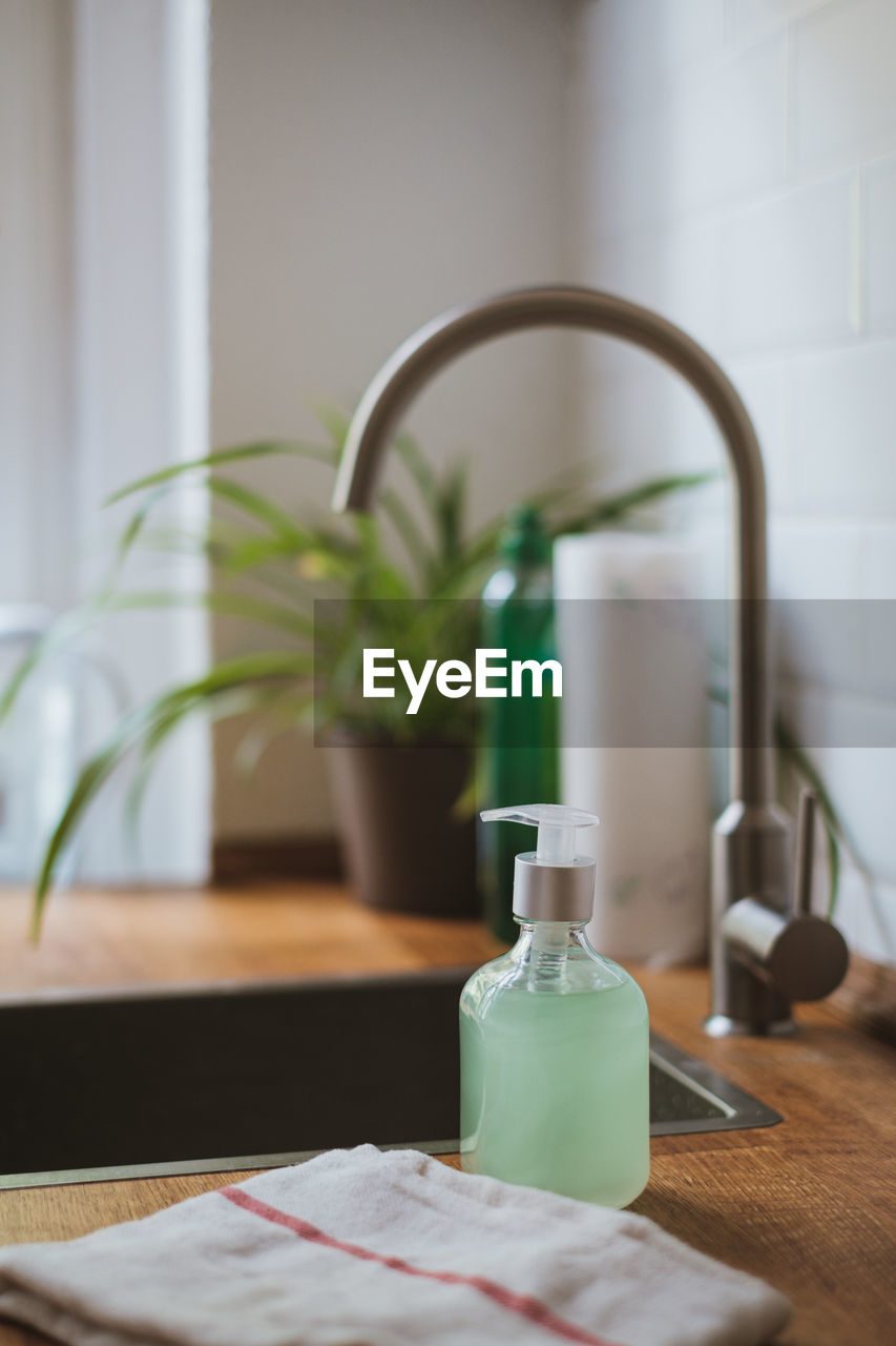 Close-up of soap bottle on kitchen counter at home with potted plant in backround