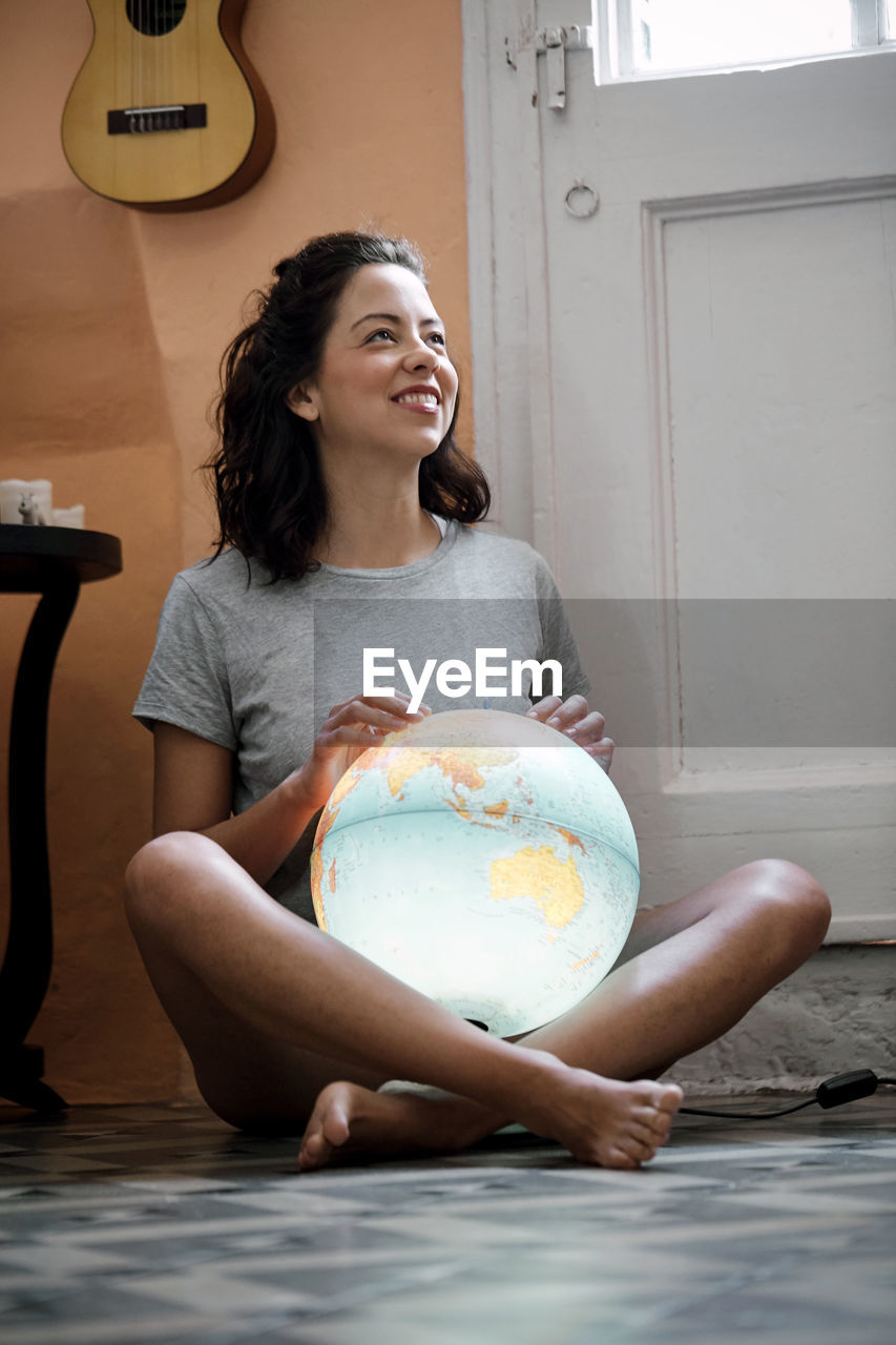 Full length of smiling woman touching globe at home