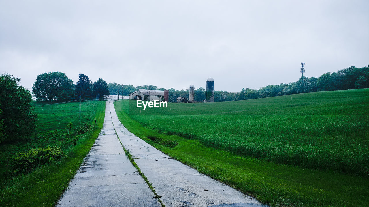 ROAD AMIDST FIELD AND TREES AGAINST SKY