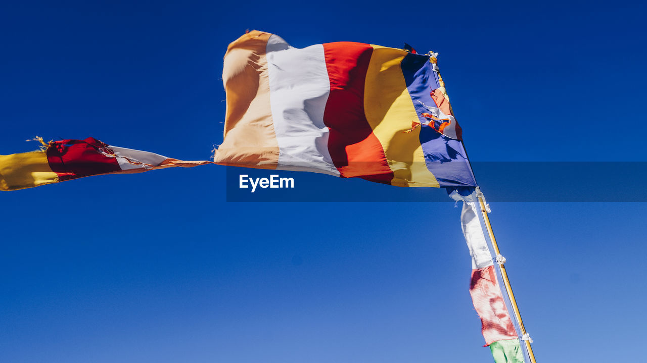 Low angle view of flag against clear blue sky on sunny day