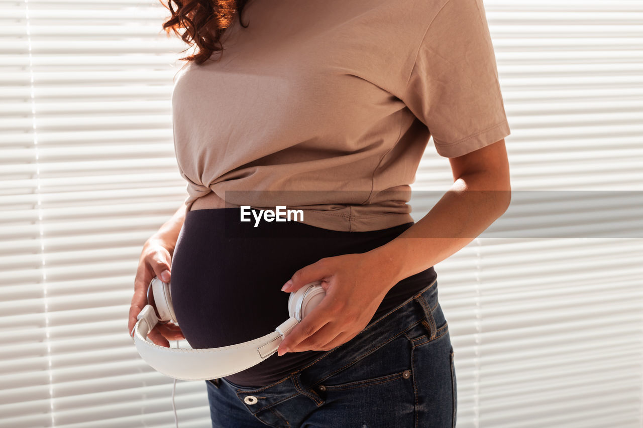 Midsection of pregnant woman holding headphones