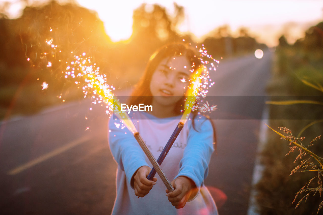 Portrait of teenage girl holding fireworks on road