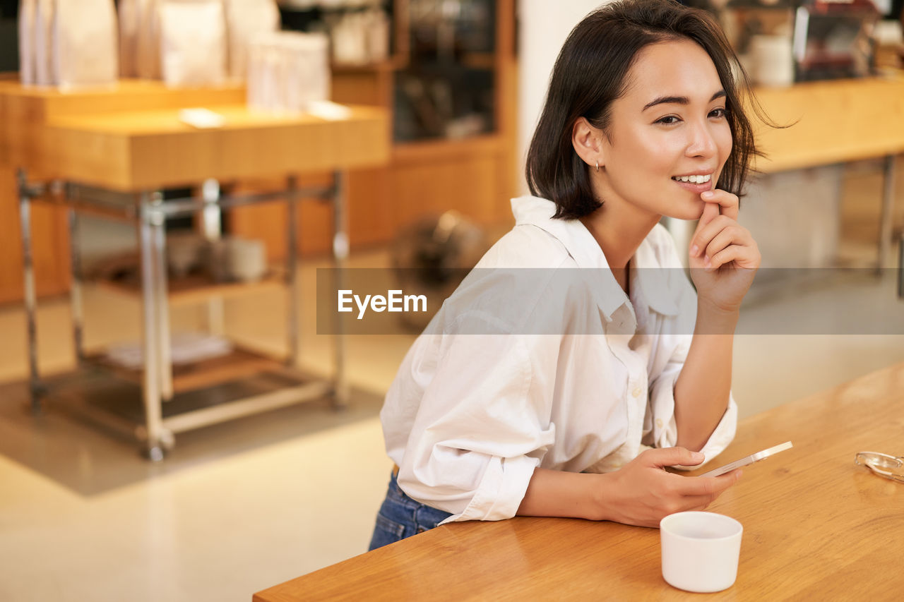 young woman using mobile phone while sitting in cafe